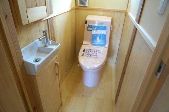 トヒバ材の床に腰壁を張ったトイレ空間。手洗い収納の造作と壁厚収納を設置