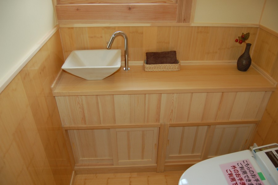 竹のフロアに竹の腰壁を張ったトイレ。造作収納に手洗い器を付けた広めのトイレ空間。便器はタンクレスですっきり。